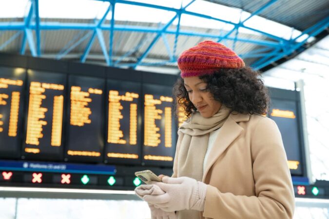Une voyageuse consulte son téléphone devant un panneau d'affichage dans une gare pour activer une eSIM Holafly aux USA avant son départ.